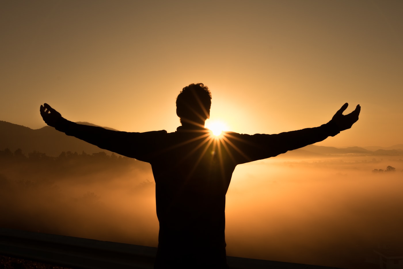 A person standing in golden sunset light with their arms open toward the horizon.