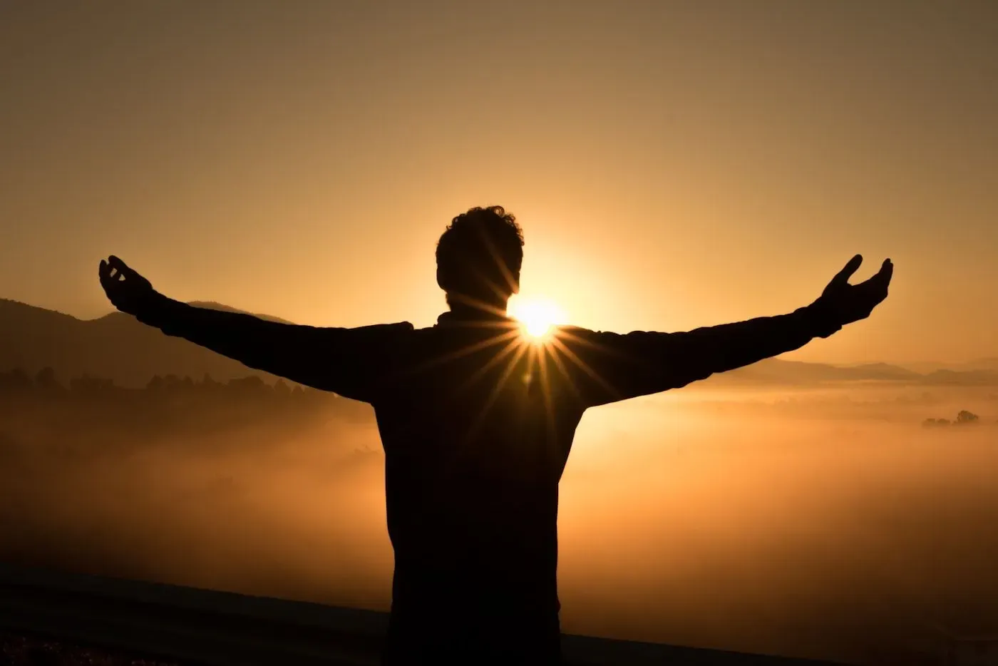 A person standing in golden sunset light with their arms open toward the horizon.